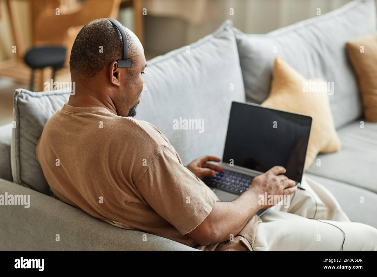 Back view at adult black man using laptop with headset while working in online meeting from home, copy space Stock Photo