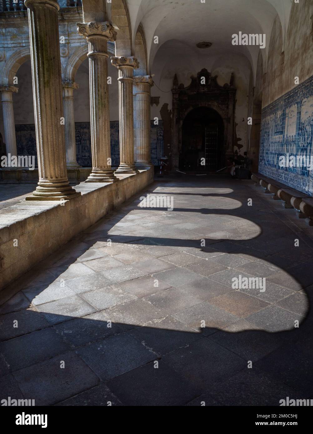 Ornate medieval arches that generate their own shadow and silhouette. Behind the cloister and the blue tile panels that cover the walls of the cloiste Stock Photo