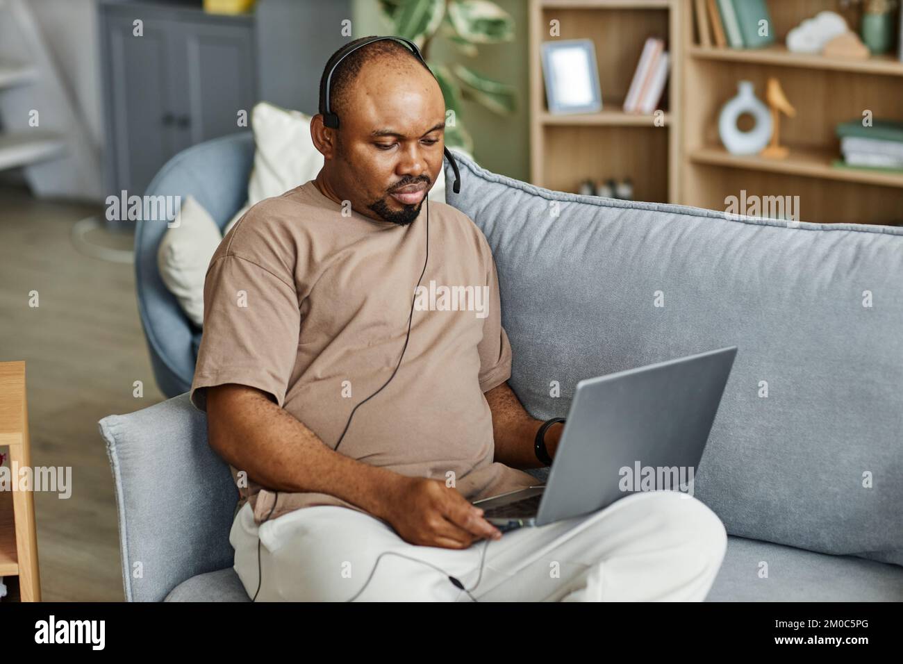 Portrait of black man using laptop with headset while working from home in online meeting, copy space Stock Photo