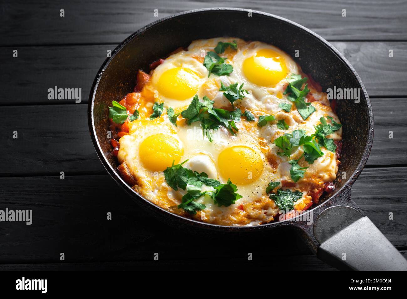 Pan of fried eggs and tomatoes on a dark table surface, top view. Egg ...