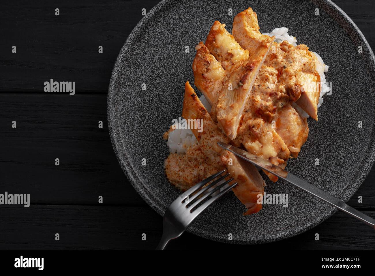 A man is eating an Indian dish. Hands holding knife and fork. Indian chicken with butter and basmati rice in a plate. .Black background. Place for Stock Photo