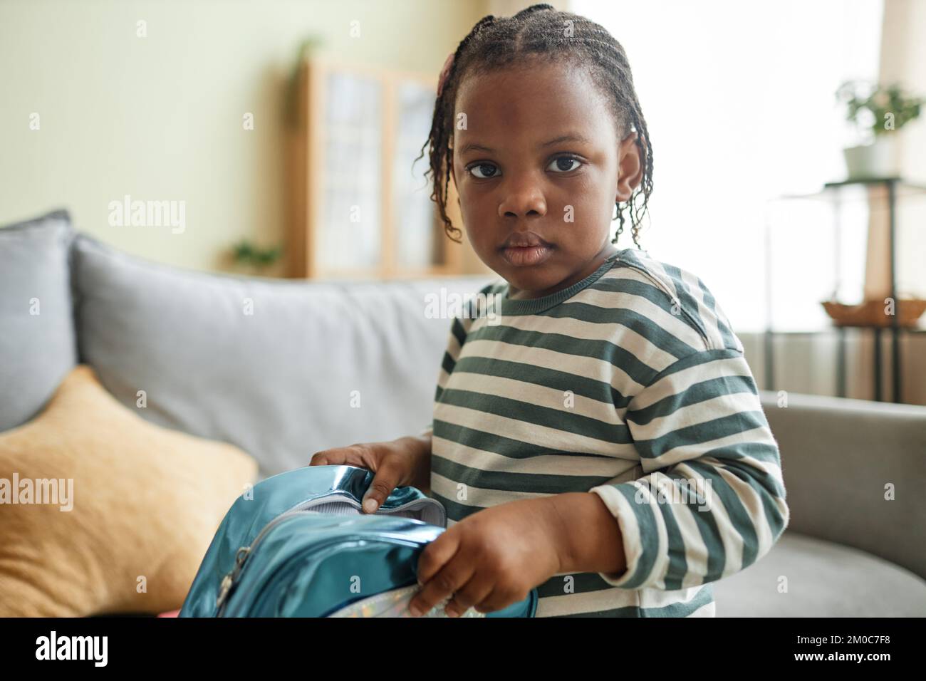 Close up portrait of cute black child looking at camera in cozy home setting and holding bag with toys, copy space Stock Photo