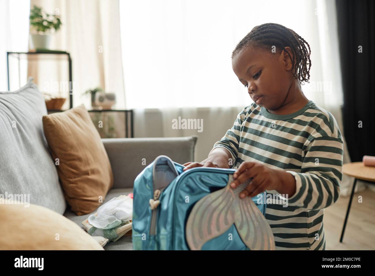 Portrait of cute black kid playing with toy bag in cozy home setting packing for nursery school, copy space Stock Photo