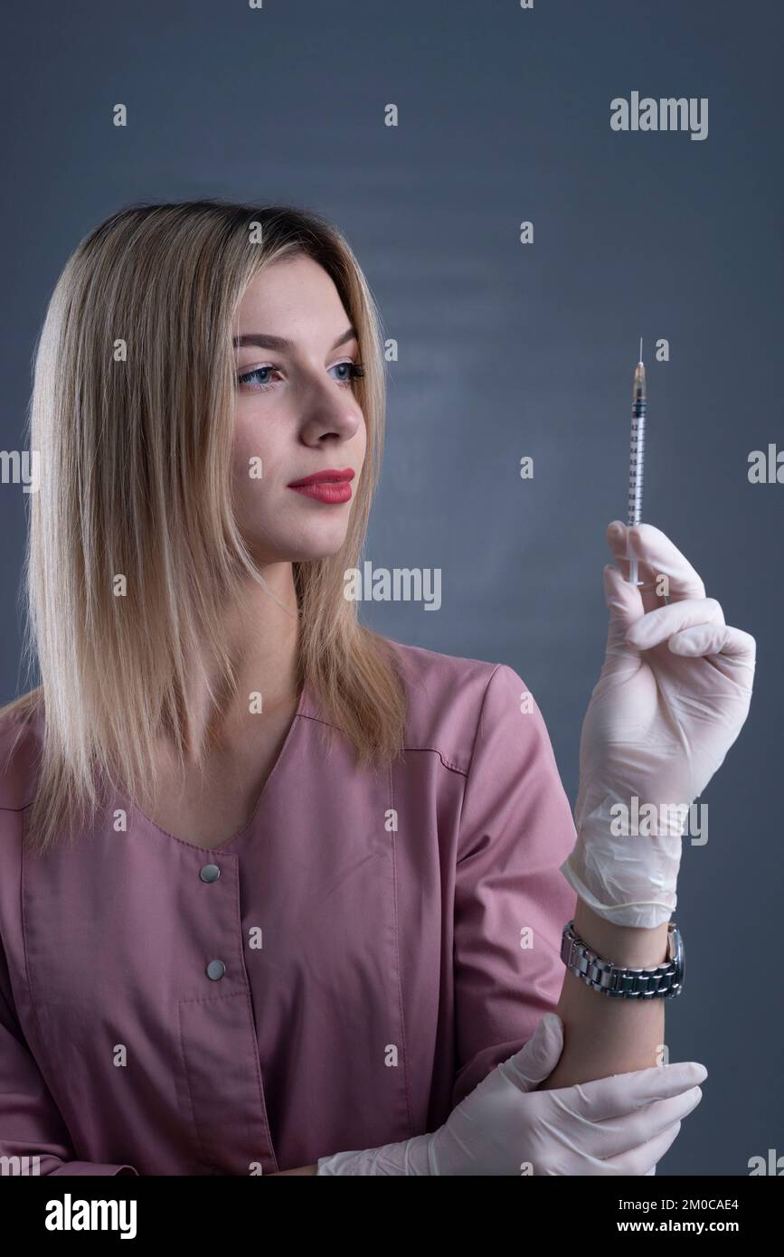 girl cosmetologist holds a syringe in her hand on a gray background. Stock Photo