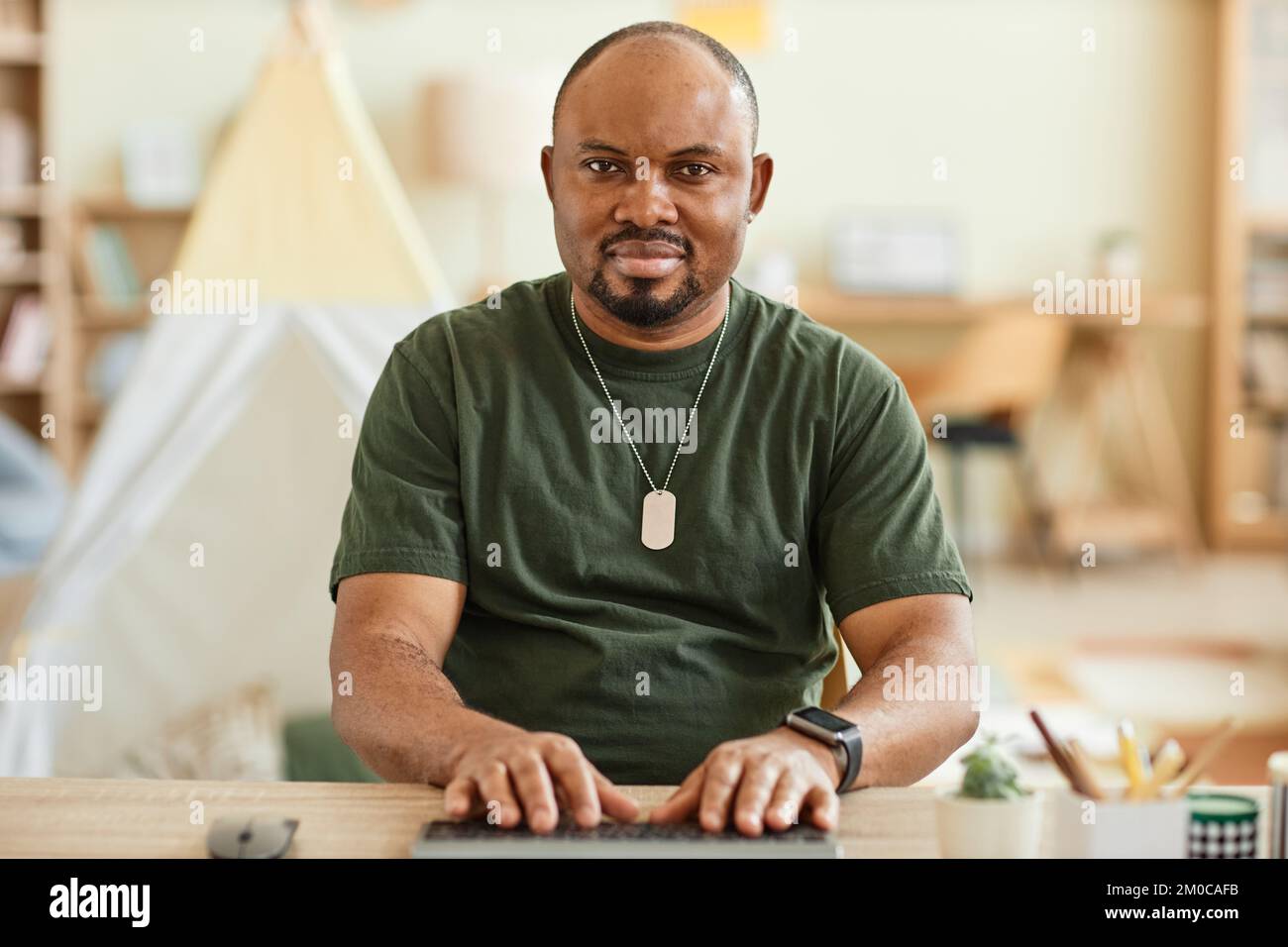 Warm toned portrait of adult black man using computer at home and looking at camera POV Stock Photo