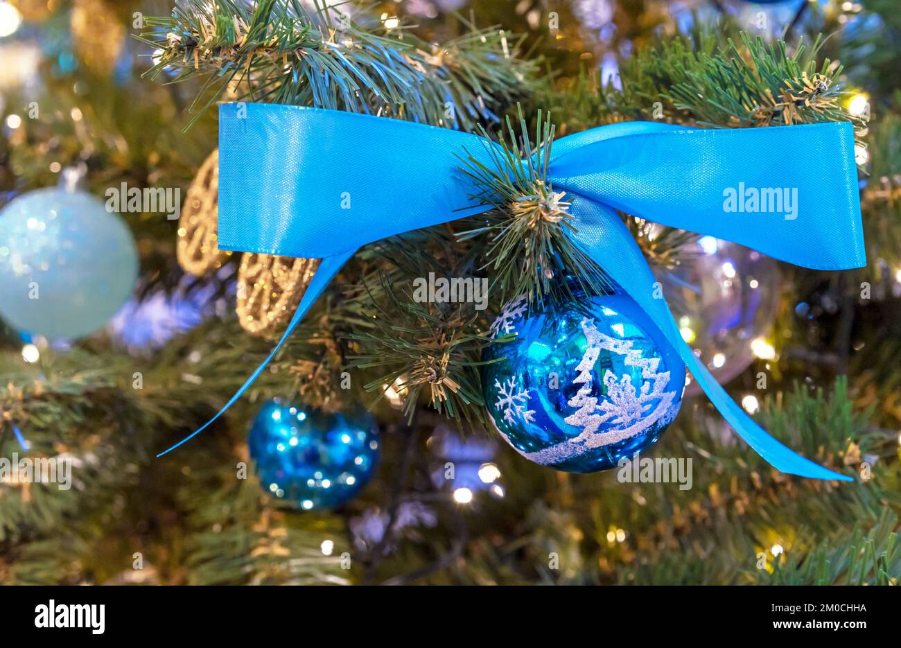 Blue Christmas ball with a blue satin ribbon on the Christmas tree. Stock Photo