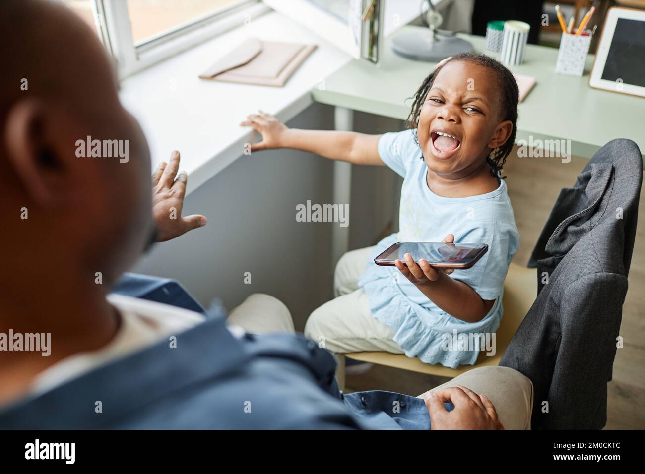 High angle portrait of black little girl screaming at father trying to take away smartphone Stock Photo