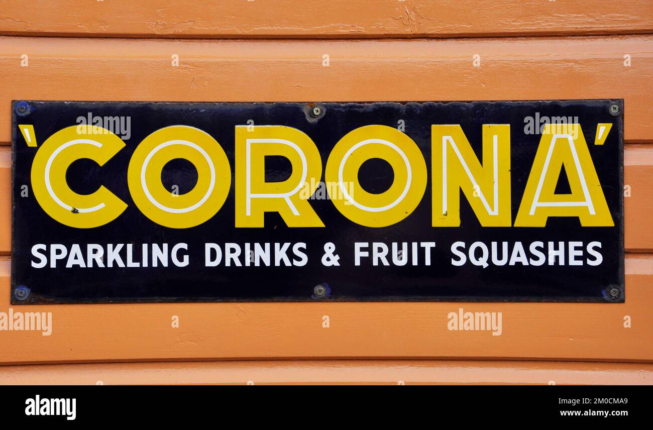 Enamelled metal sign, advertising Corona sparkling drinks and fruit squashes photographed at Bishops Lydeard station on the West Somerset railway in S Stock Photo