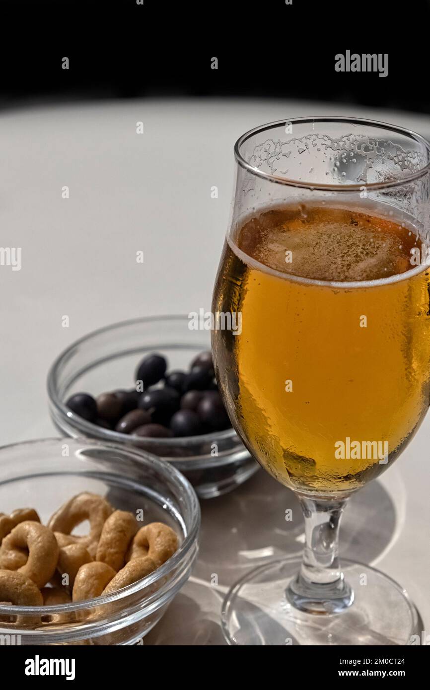 Glass of lager beer with olives and Taralli biscuit snacks on a table