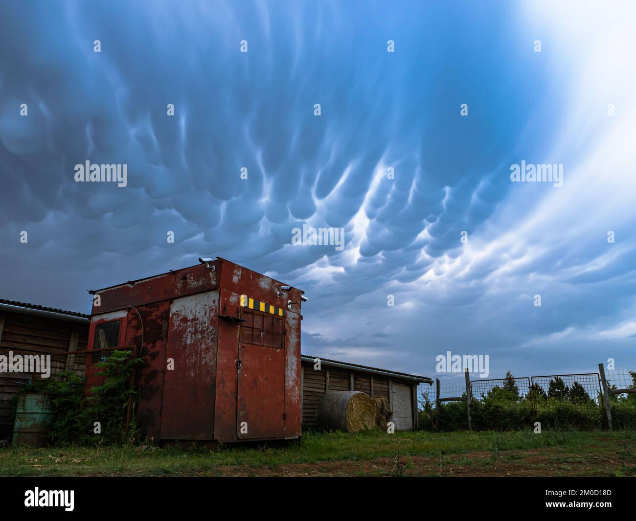 Red barn building container house before thunderstorm, dramatic sky with mammatus clouds Stock Photo