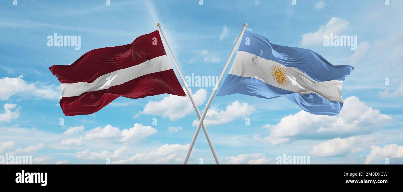 two crossed flags Argentina and Latvia waving in wind at cloudy sky ...