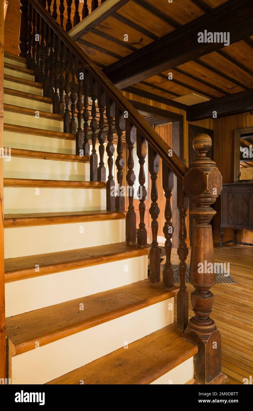 Pine wood stairs with turned newel post and railing leading to upstairs floor inside old 1826 Canadiana cottage style home. Stock Photo