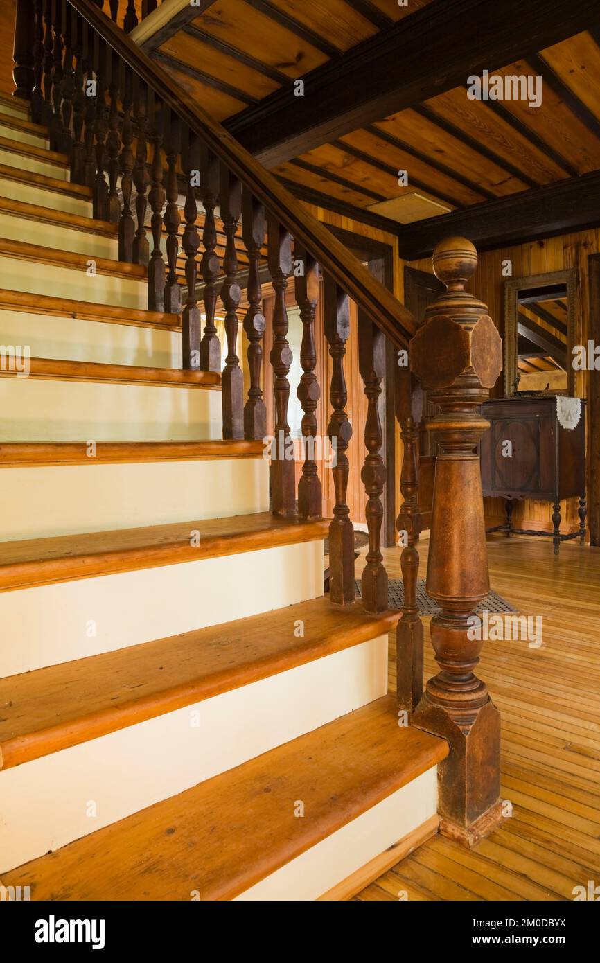 Pine wood stairs with turned newel post and railing leading to upstairs floor inside old 1826 Canadiana cottage style home. Stock Photo