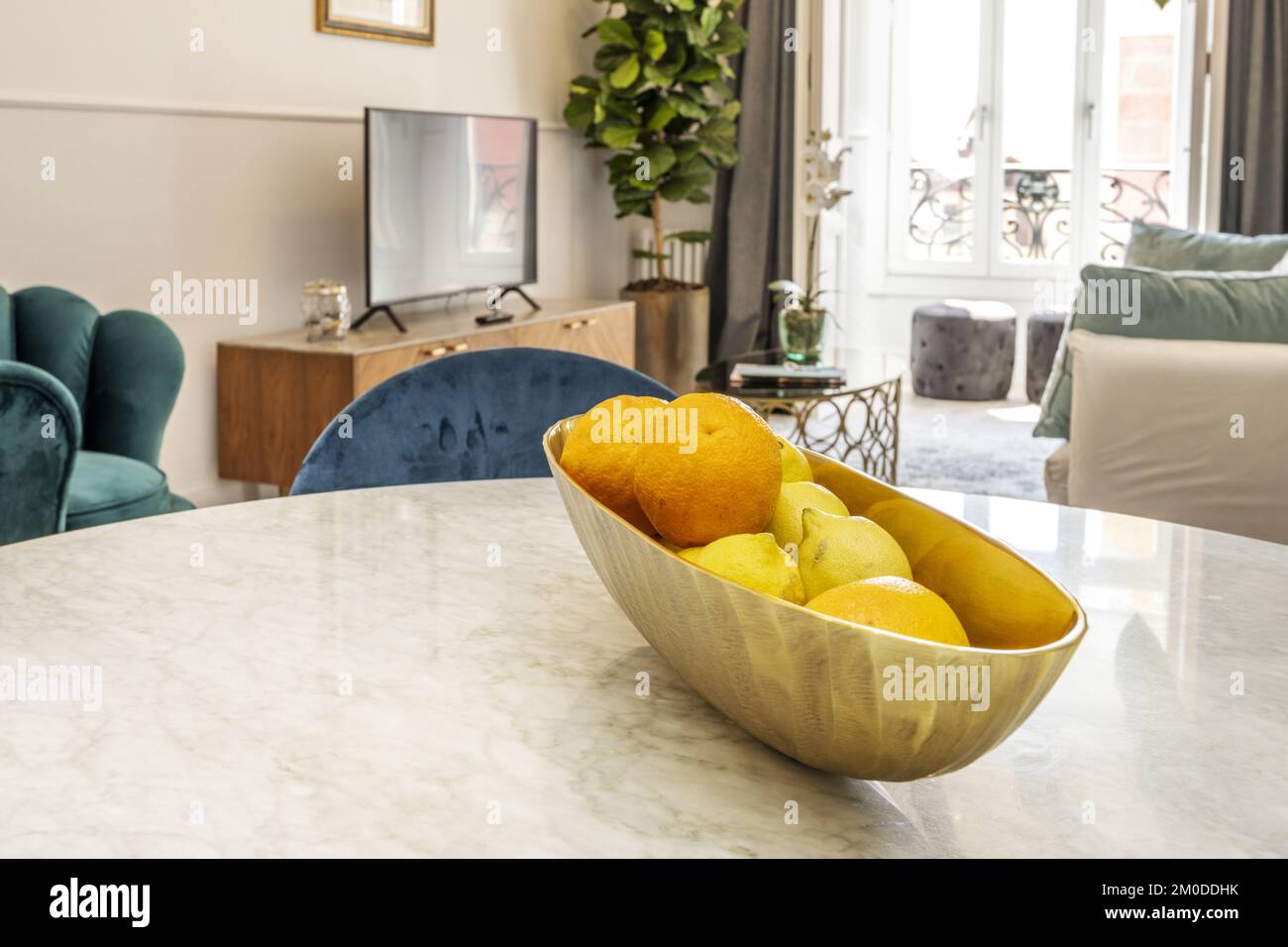 An elongated polished brass centerpiece filled with oranges and lemons on a circular polished white marble table Stock Photo