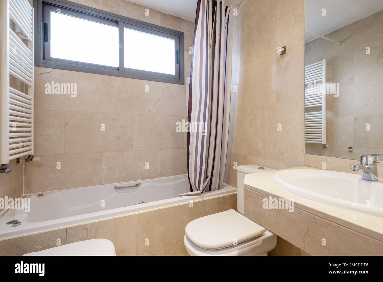 A bathroom with cream marble tiles, a bathtub with hydromassage jets and a frameless mirror