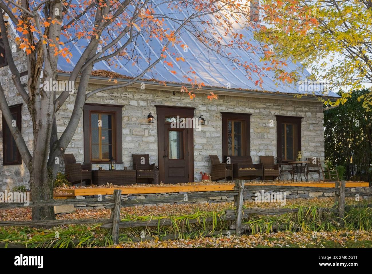 Old circa 1750 Canadiana cottage style fieldstone home with silver sheet metal roof in autumn. Stock Photo