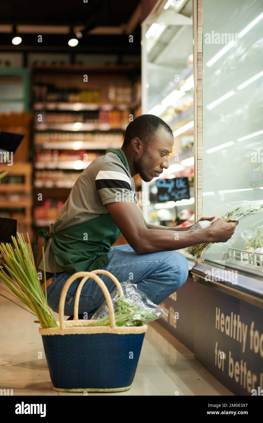 Grocery store worker checking expiration date on packages of greens