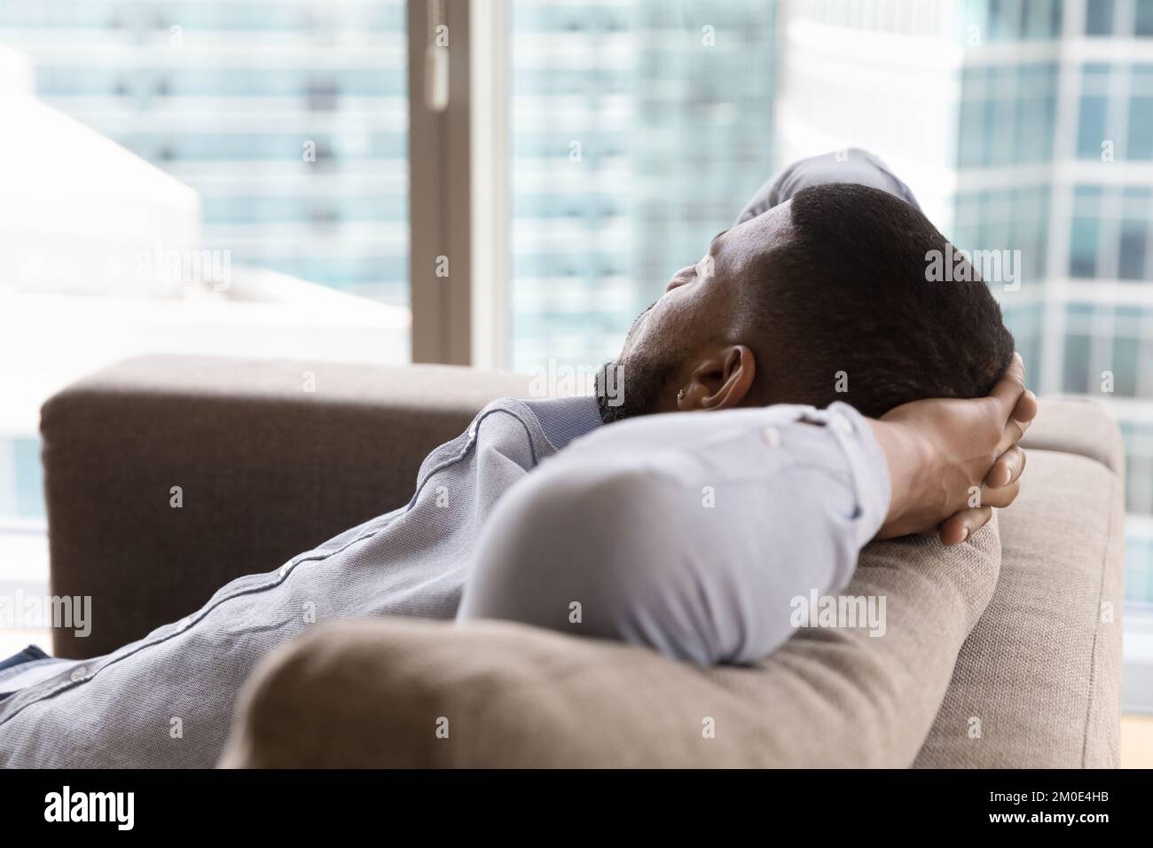 Dreamy sleepy young Black man relaxing on couch Stock Photo