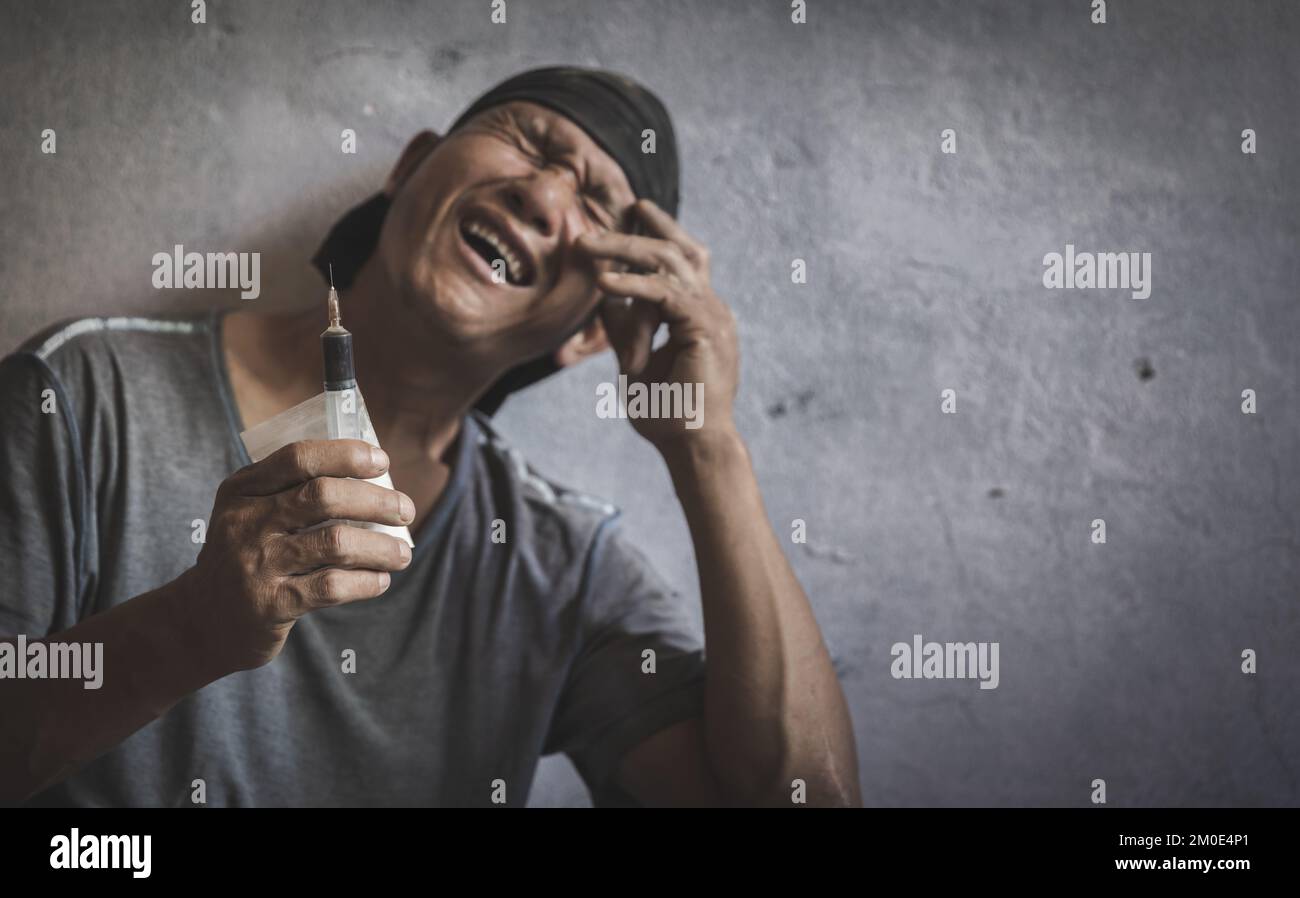 Drug addict holding a syringe about to inject intravenously.Anti-drug concept. Addicted man. Syringe.Despair.Despair.The young man is very stressed. H Stock Photo