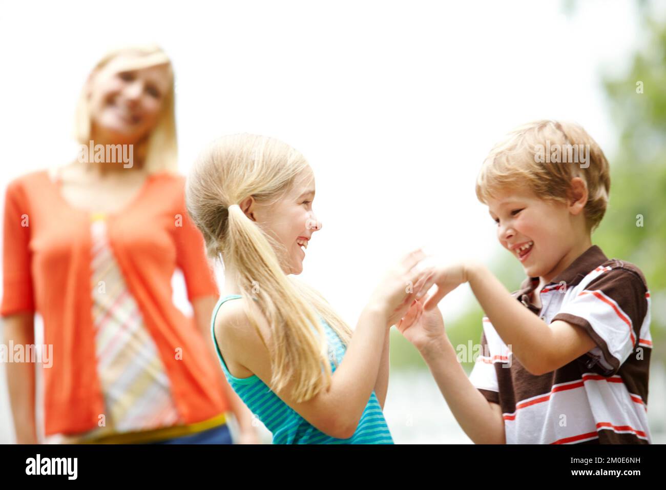 Playing together while relaxing with mom. Two cute young children spending time outdoors with their mother. Stock Photo