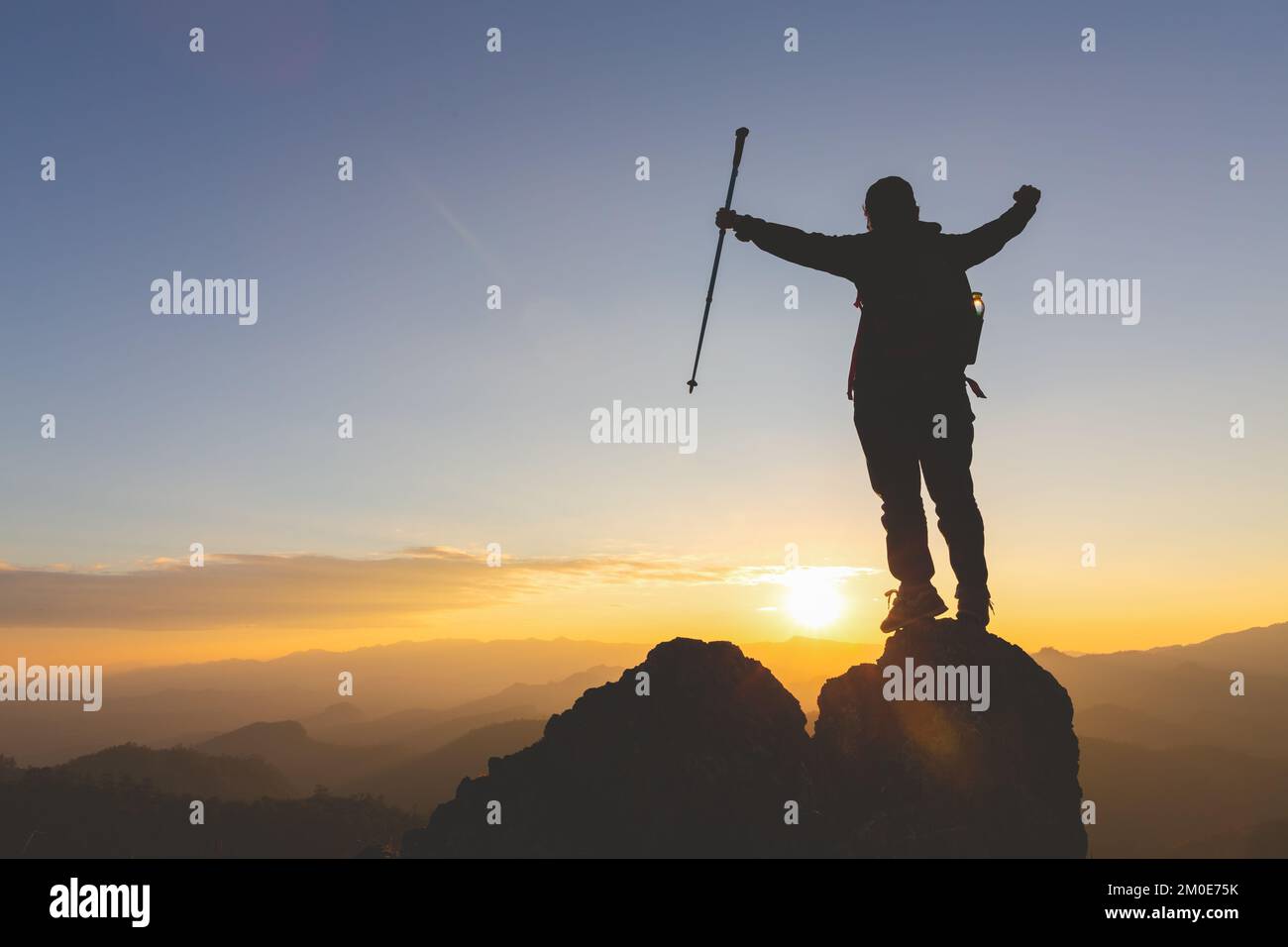 Silhouette of young woman standing alone on top of mountain and raise ...