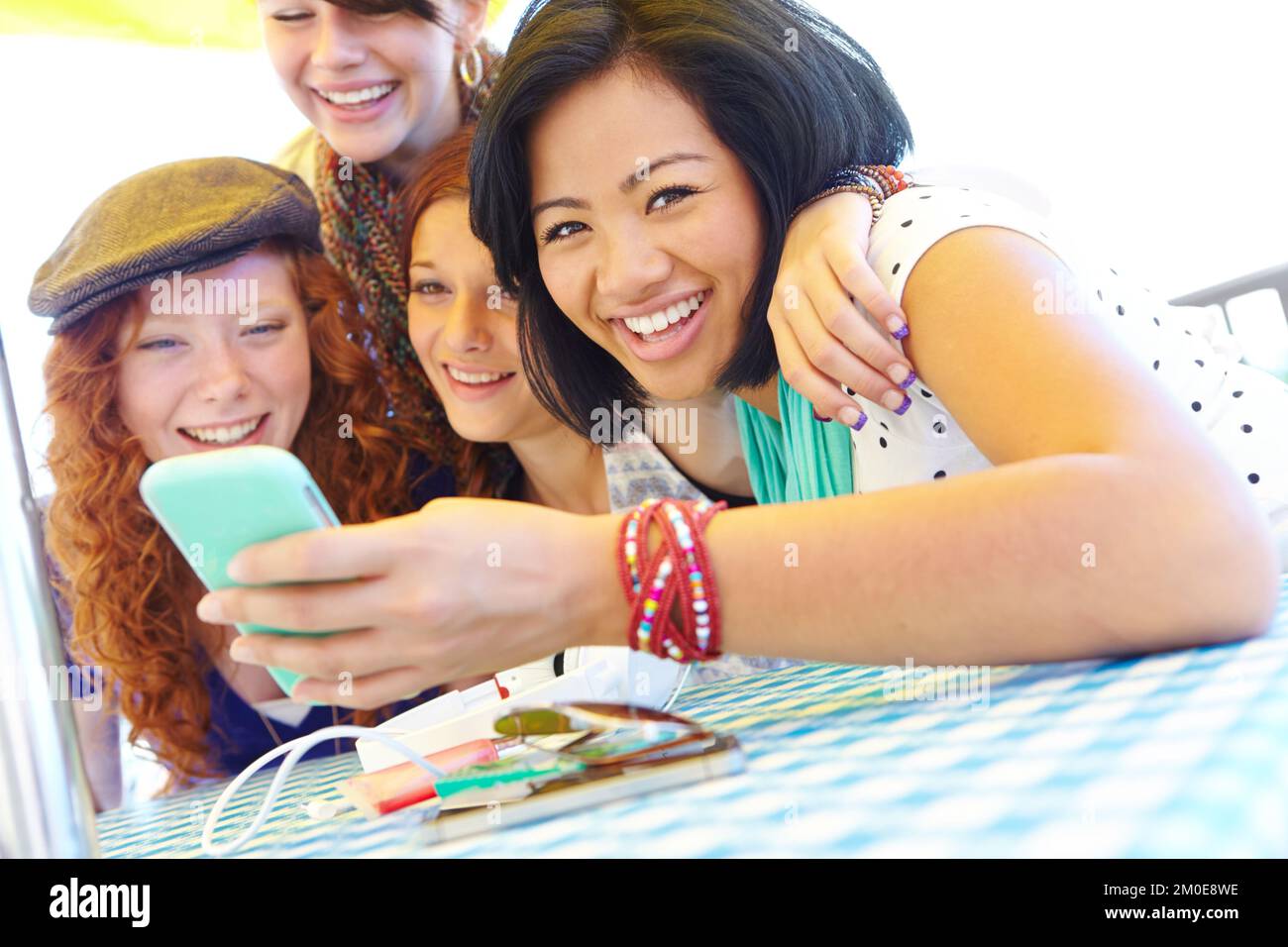 Sharing the latest news. A group of adolescent girls laughing as they look at something on a smartphone screen. Stock Photo