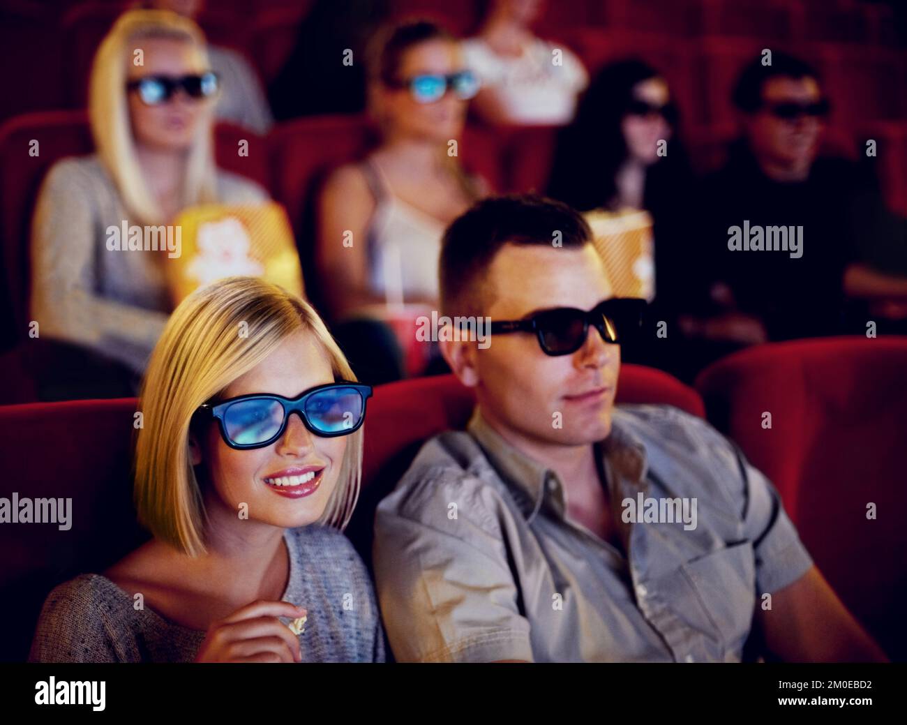 Something we like to share. A couple sitting and eating popcorn while watching a 3D movie together in a cinema. Stock Photo