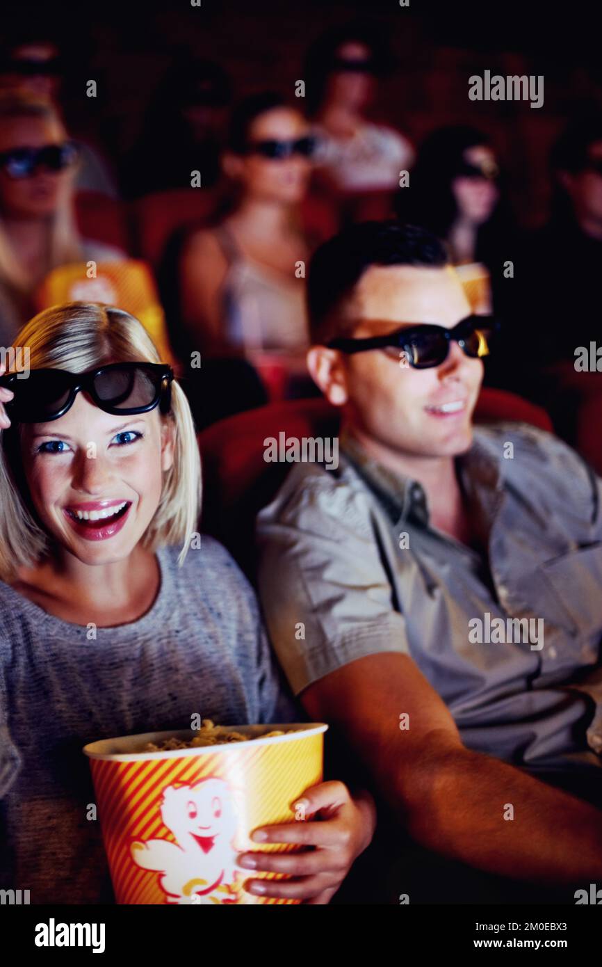 Wow Youve got to see this. A couple sitting and eating popcorn while watching a 3D movie together in a cinema. Stock Photo