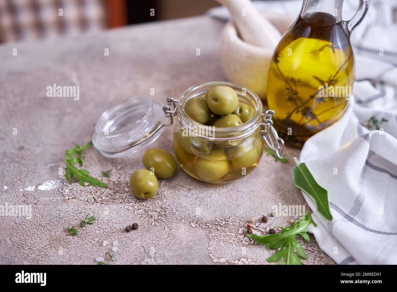 Canned green olives in a glass can and small bottle of olive oil with