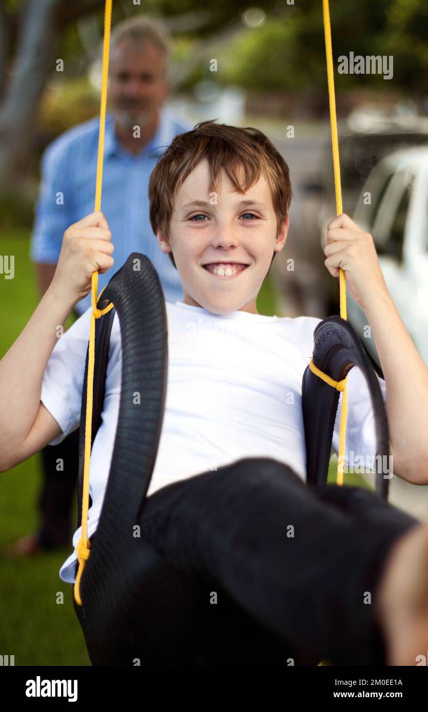 Push me higher dad. Young boy being pushed on a tyre swing by his father in the backyard. Stock Photo