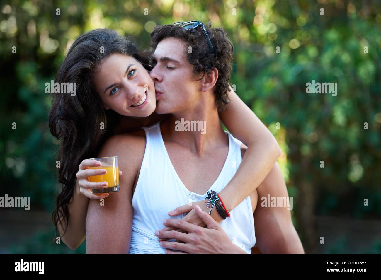 So comfortable with one another. Cute young woman being kissed by her boyfriend as she embraces him - portrait. Stock Photo