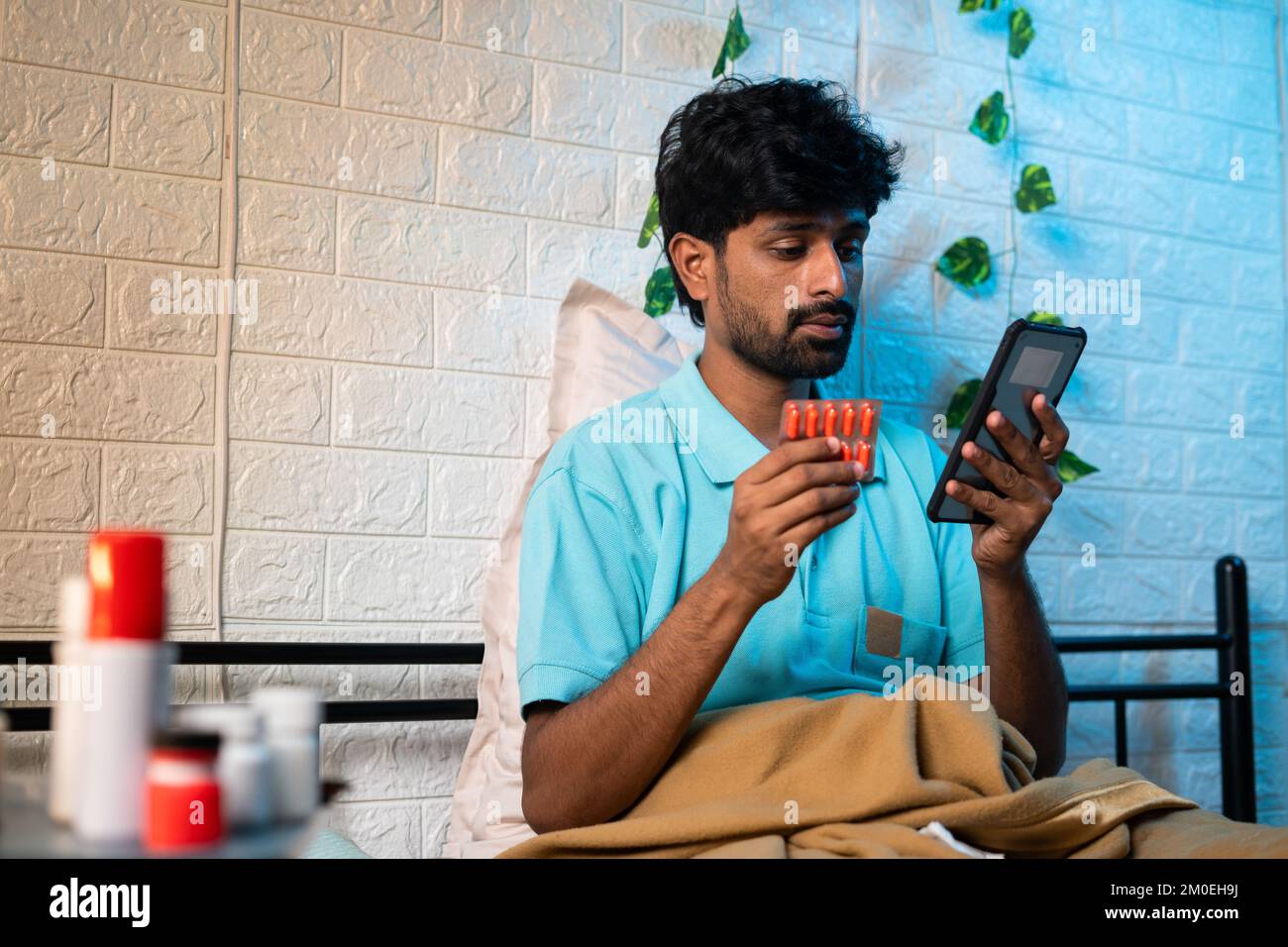 Young man ordering online medicine on mobile phone while sitting at bedroom - concept of E pharmacy, healthcare and technology Stock Photo