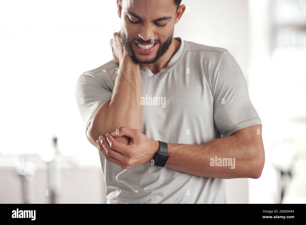 One young hispanic man holding his sore elbow while exercising in a gym