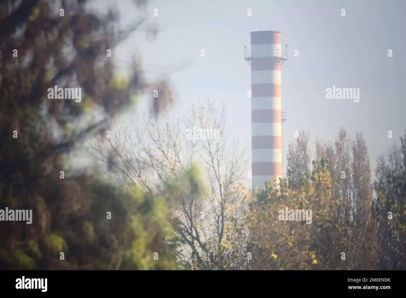 Red  and white chimney framed by trees on a misty day in autumn Stock Photo