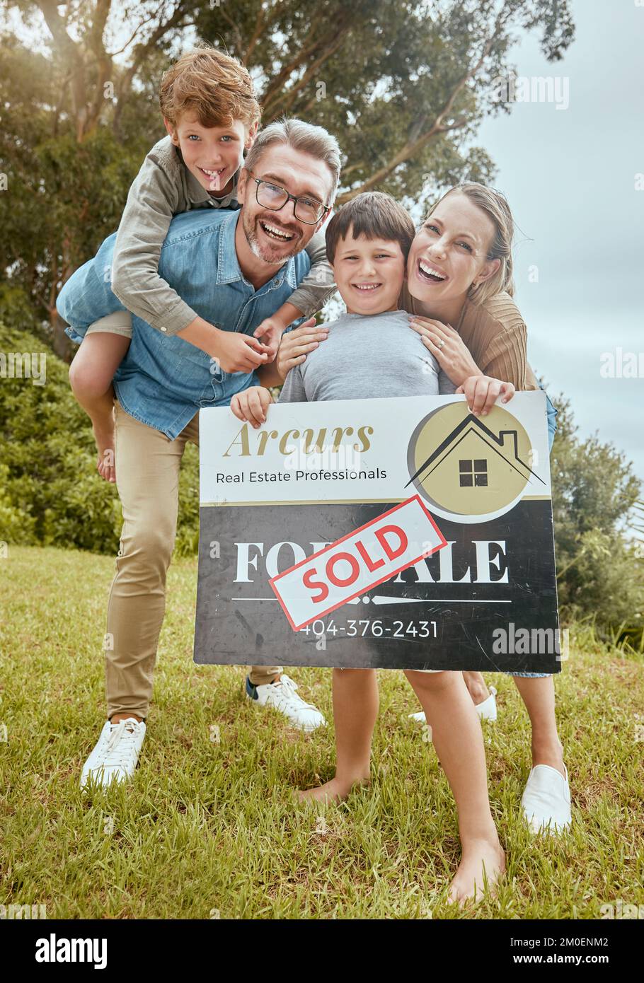 Portrait of happy caucasian family holding a sold sign while relocating and moving into a new house. Smiling parents and kids secure homeowner loan Stock Photo