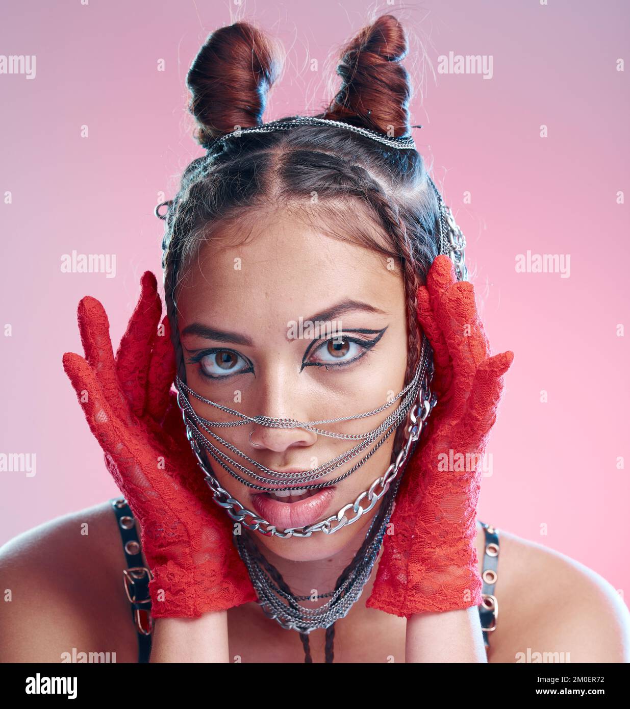 Stylish, goth and portrait of a woman with chains on her face on a pink studio background. Front, headshot and edgy fashion female with chain or metal Stock Photo
