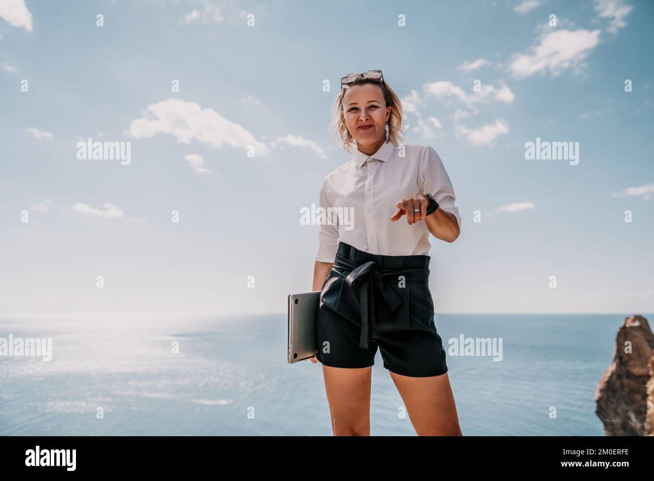 Digital nomad, Business woman working on laptop by the sea. Pretty lady typing on computer by the sea at sunset, makes a business transaction online Stock Photo