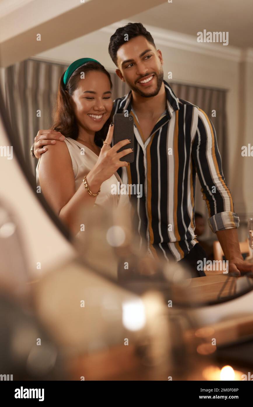 Dinner party, celebration and couple with selfie on a phone in mirror enjoy holiday, festival and Christmas party. Social event, restaurant and young Stock Photo
