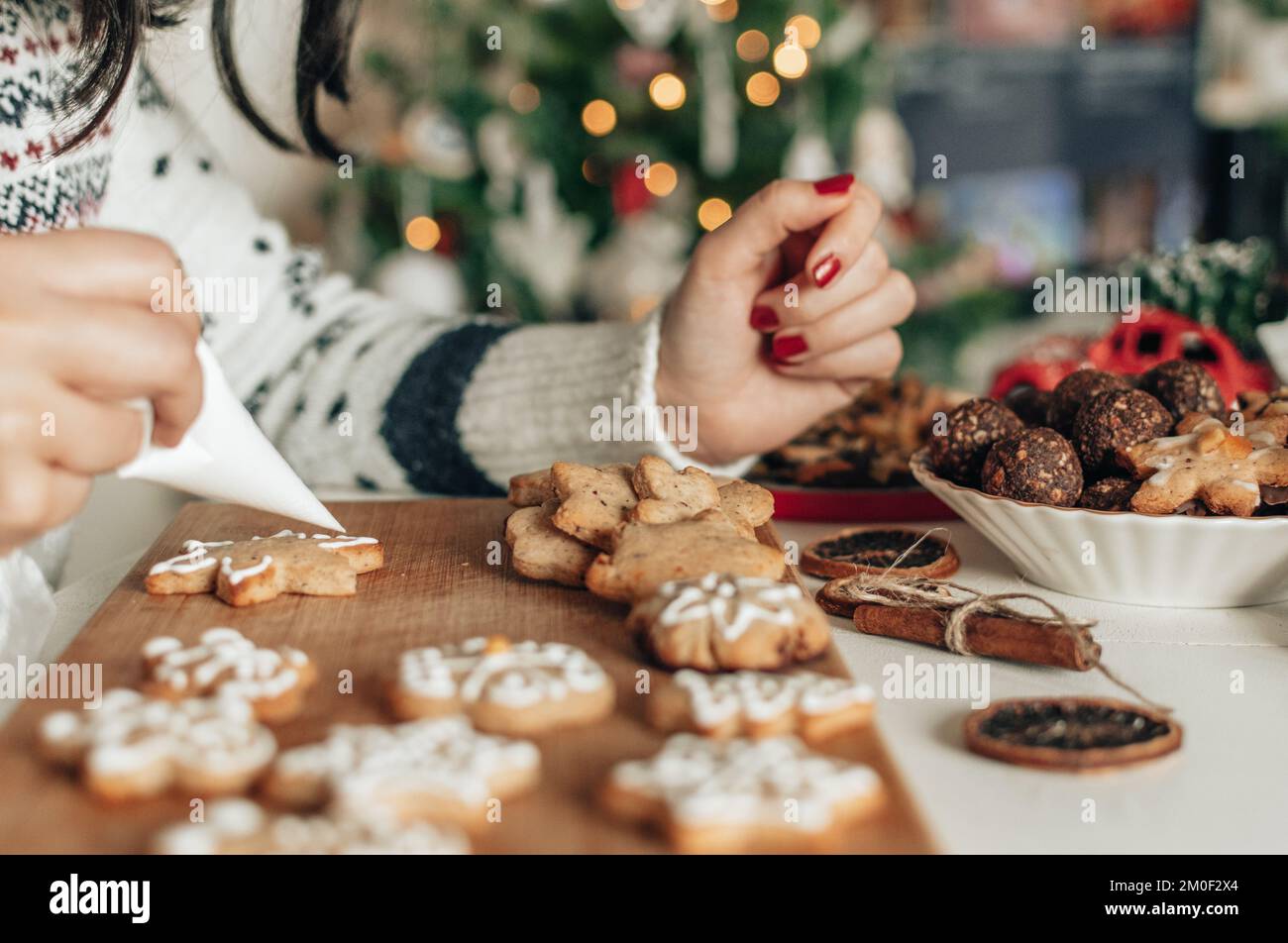 Woman holding piping bag, decorating home baked christmas cookies with