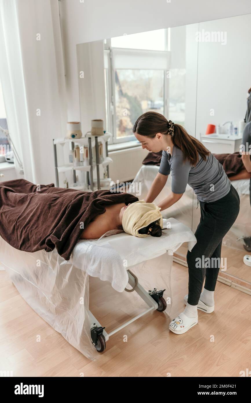 Masseuse doing anti stress body massage on woman laying on massage table wrapped in towel Stock Photo