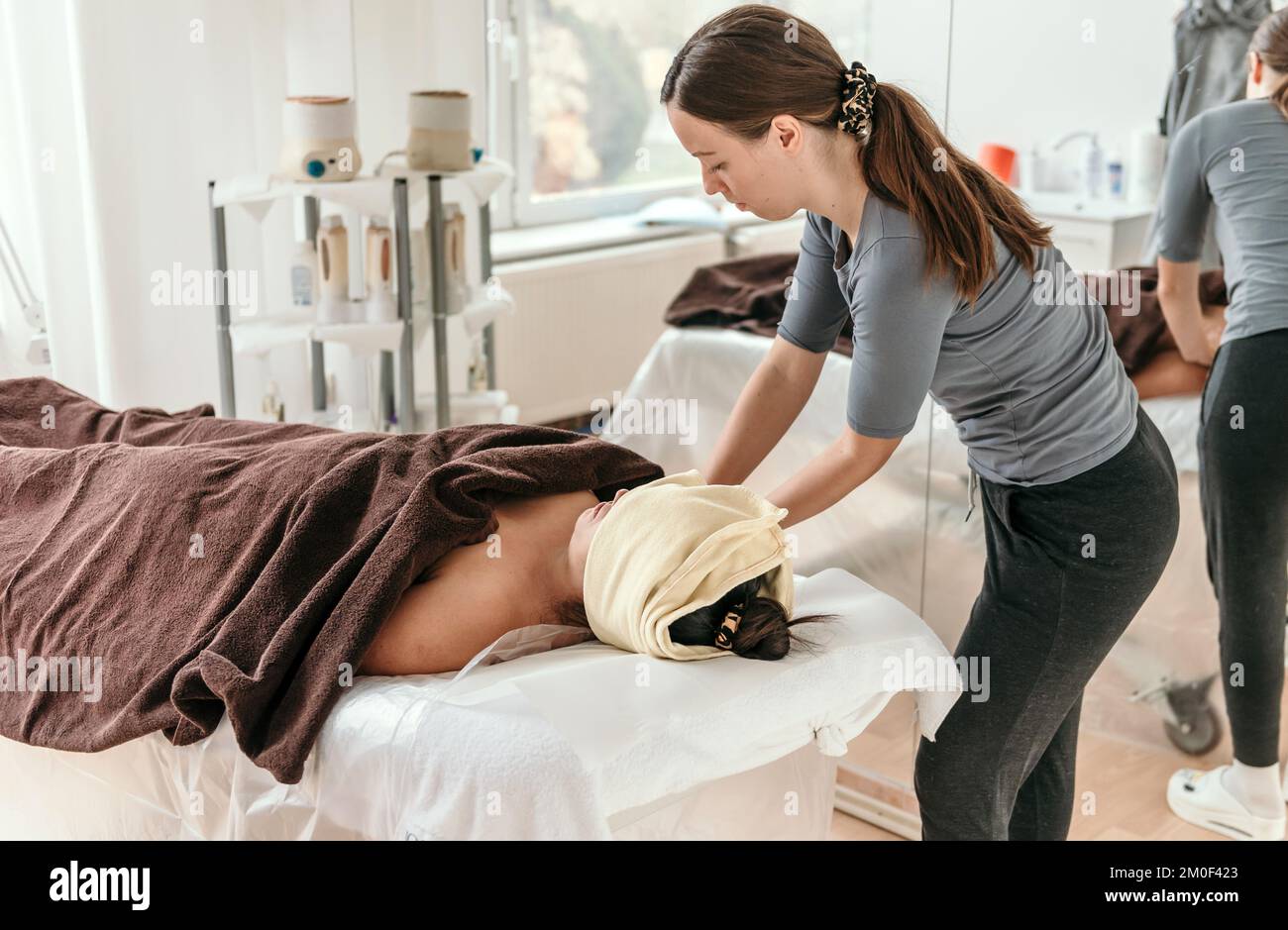 Masseuse doing anti stress body massage on woman laying on massage table wrapped in towel Stock Photo