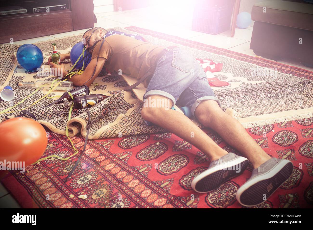 Party, drunk and hangover with a man sleeping on a living room floor after new year celebration. Beer, college and hungover with a male passed out Stock Photo