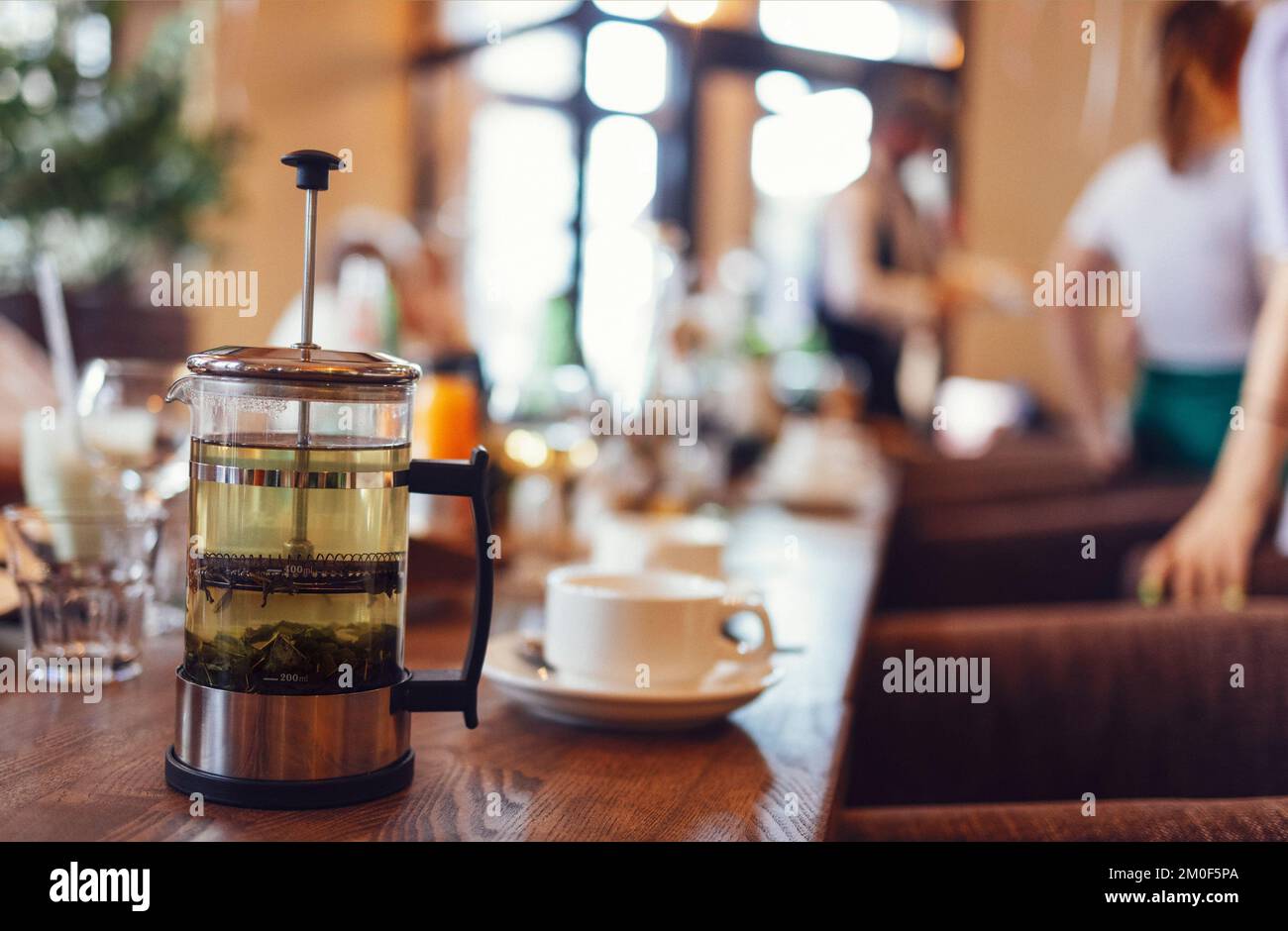 Close up of wooden table serving glass french press tea maker, cups with fresh beverage and sweet pastry on plate in cafe Stock Photo