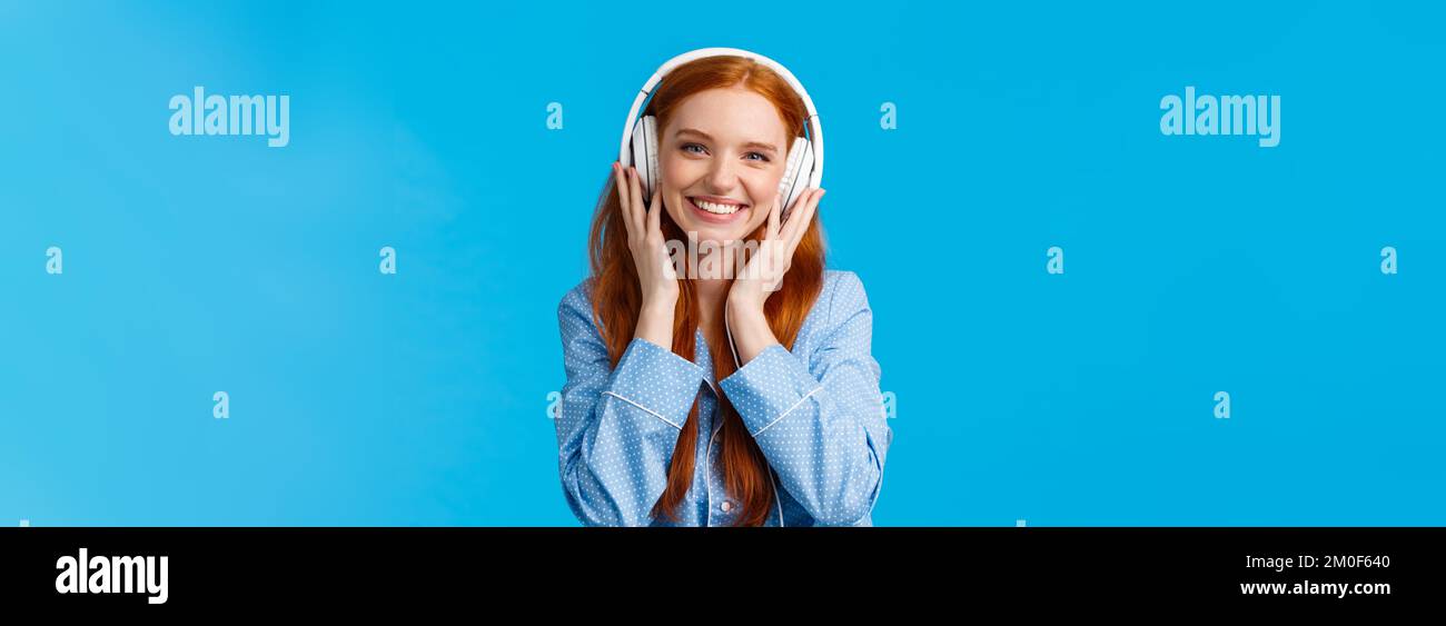 Waist-up shot cheerful pretty foxy caucasian girl listening music in large headphones, smiling pleased, checking-out friends single, wearing nightwear Stock Photo