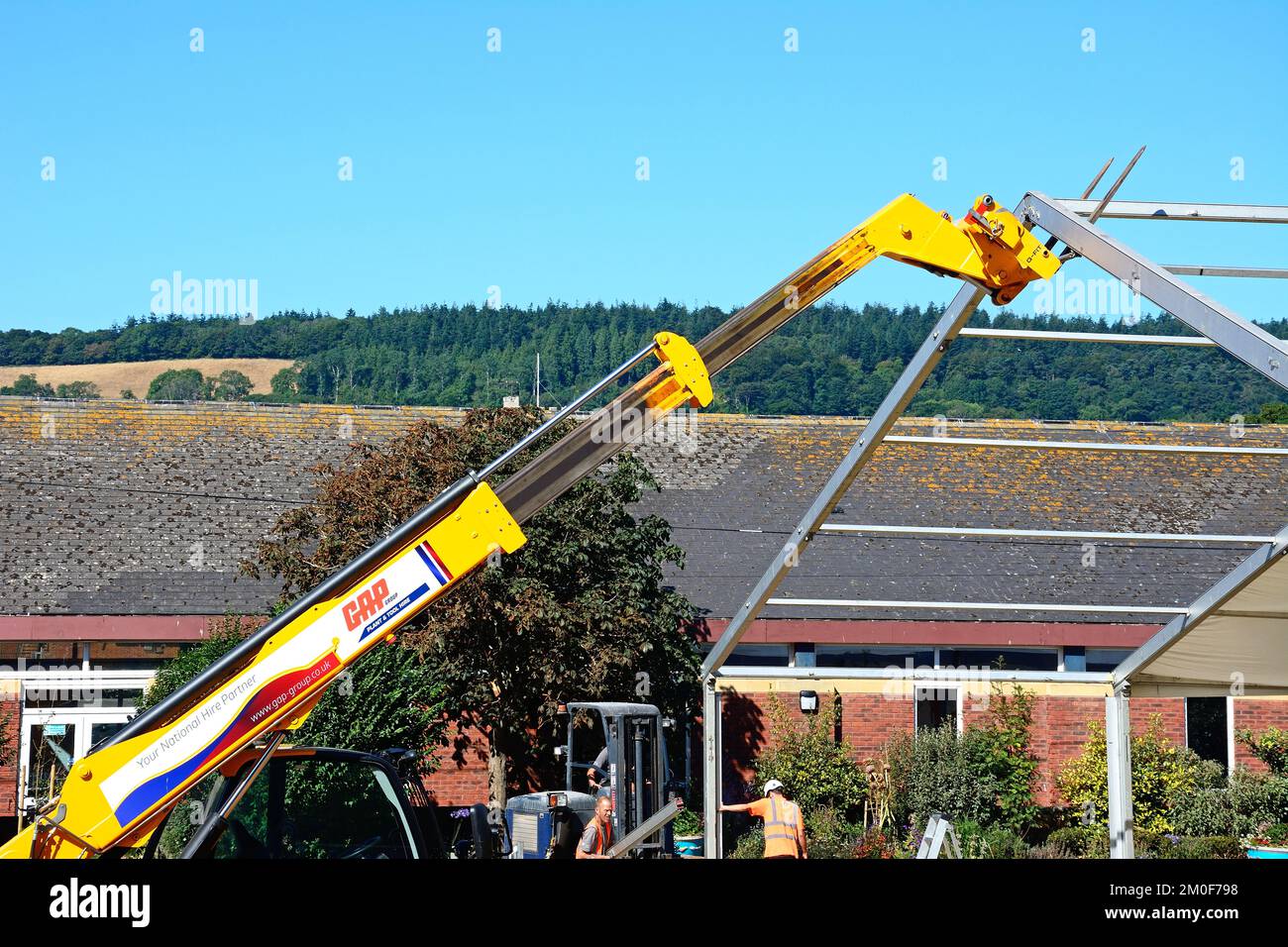 Construction workers removing metal roofing using a hydraulically powered telescopic tractor, Sidmouth, Devon, UK, Europe. Stock Photo