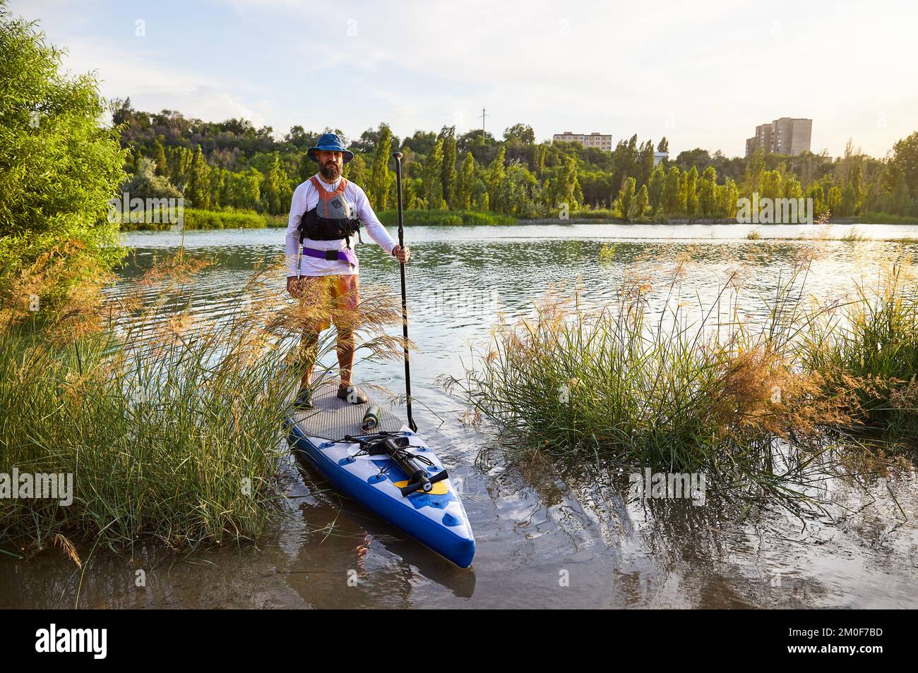 Man at stand up paddle boards SUP in the mountain lake Sairan in city Almaty in Kazakhstan. Stock Photo