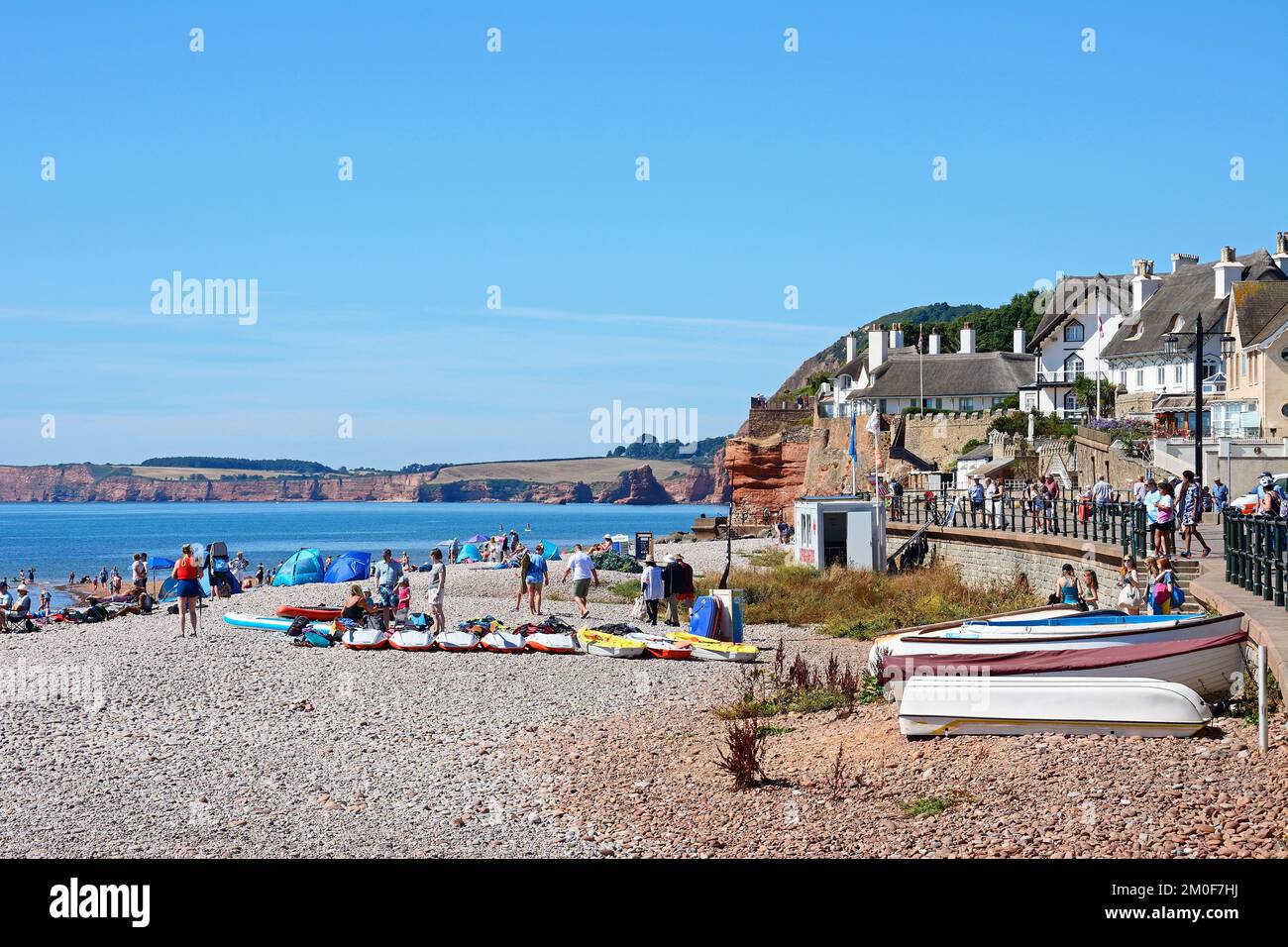 Tourists relaxing on the beach and promenade with views towards the sea and cliffs, Sidmouth, Devon, UK, Europe. Stock Photo