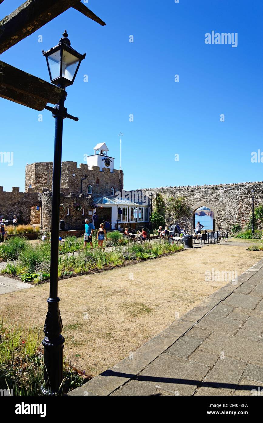 Tourists relaxing in the Connaught Gardens with a pavement cafe to the rear and views through the arch of the sea and coastline, Sidmouth, Devon, UK. Stock Photo