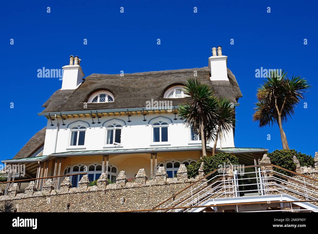 View of a traditional thatched house overlooking the beach with yuccas in the foreground, Sidmouth, Devon, UK, Europe Stock Photo