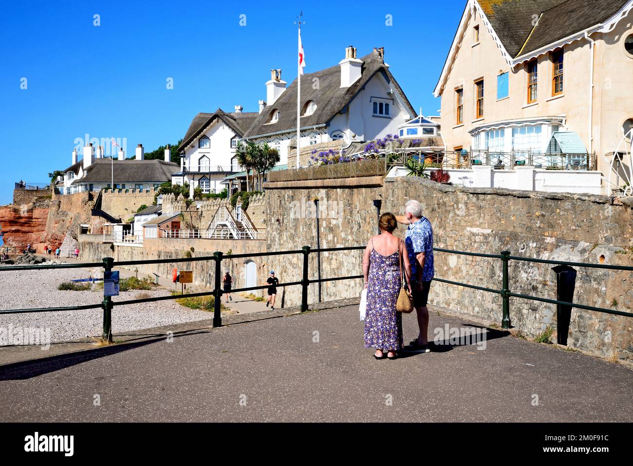 View of traditional thatched houses overlooking the beach at the West End of the town with a couple standing in the foreground, Sidmouth, Devon, UK. Stock Photo